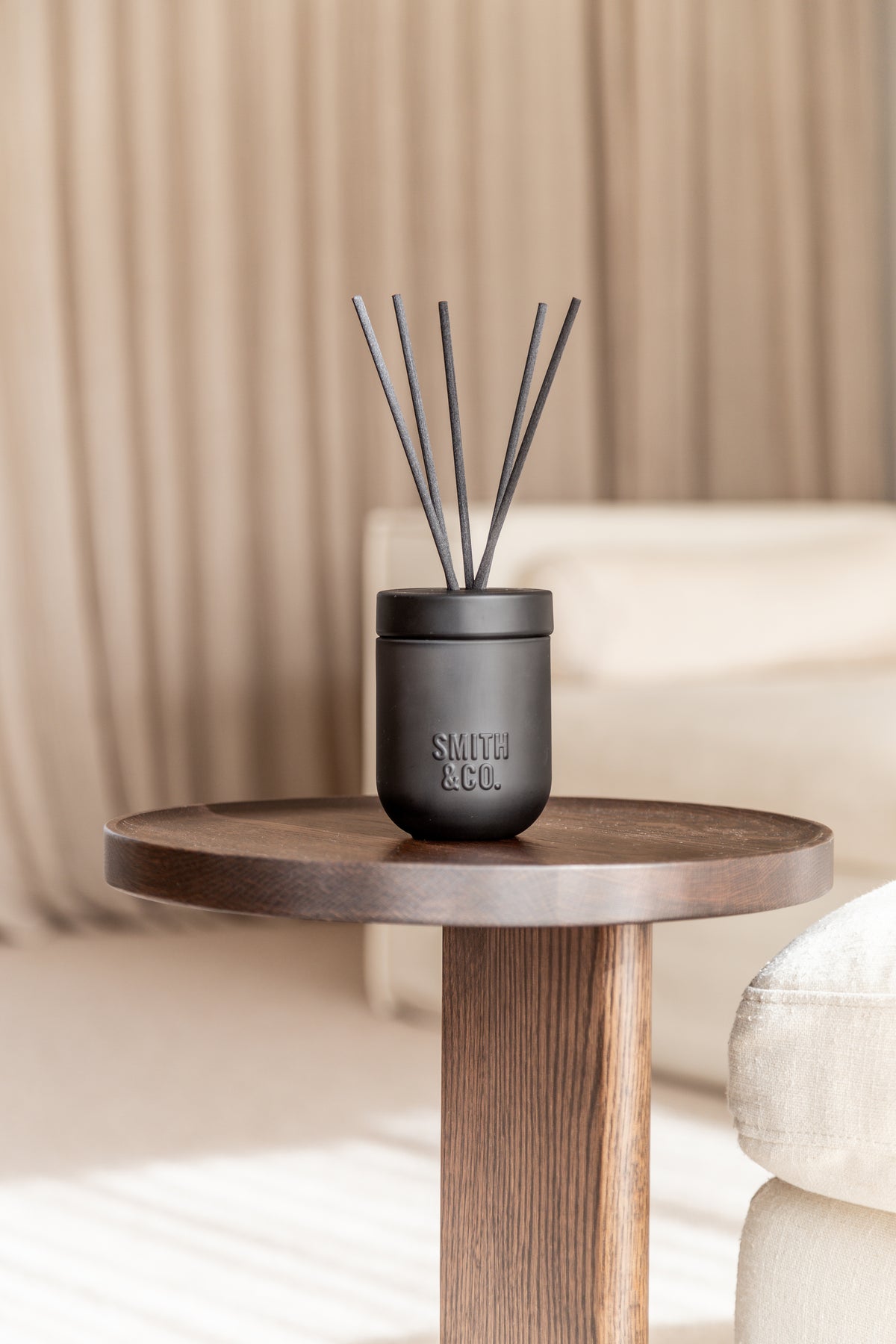 Smith & Co. diffuser on a round timber side table beside a sofa and curtains