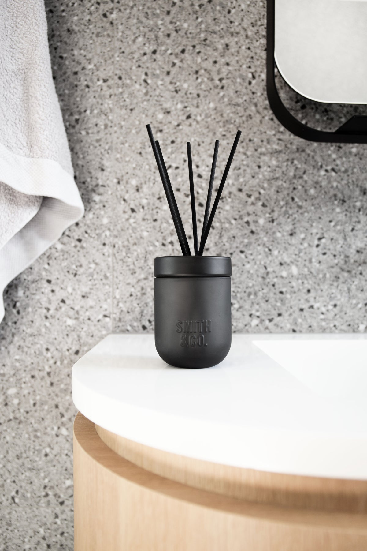 Smith & Co. diffuser on a curved white vanity below a round mirror, terrazzo behind