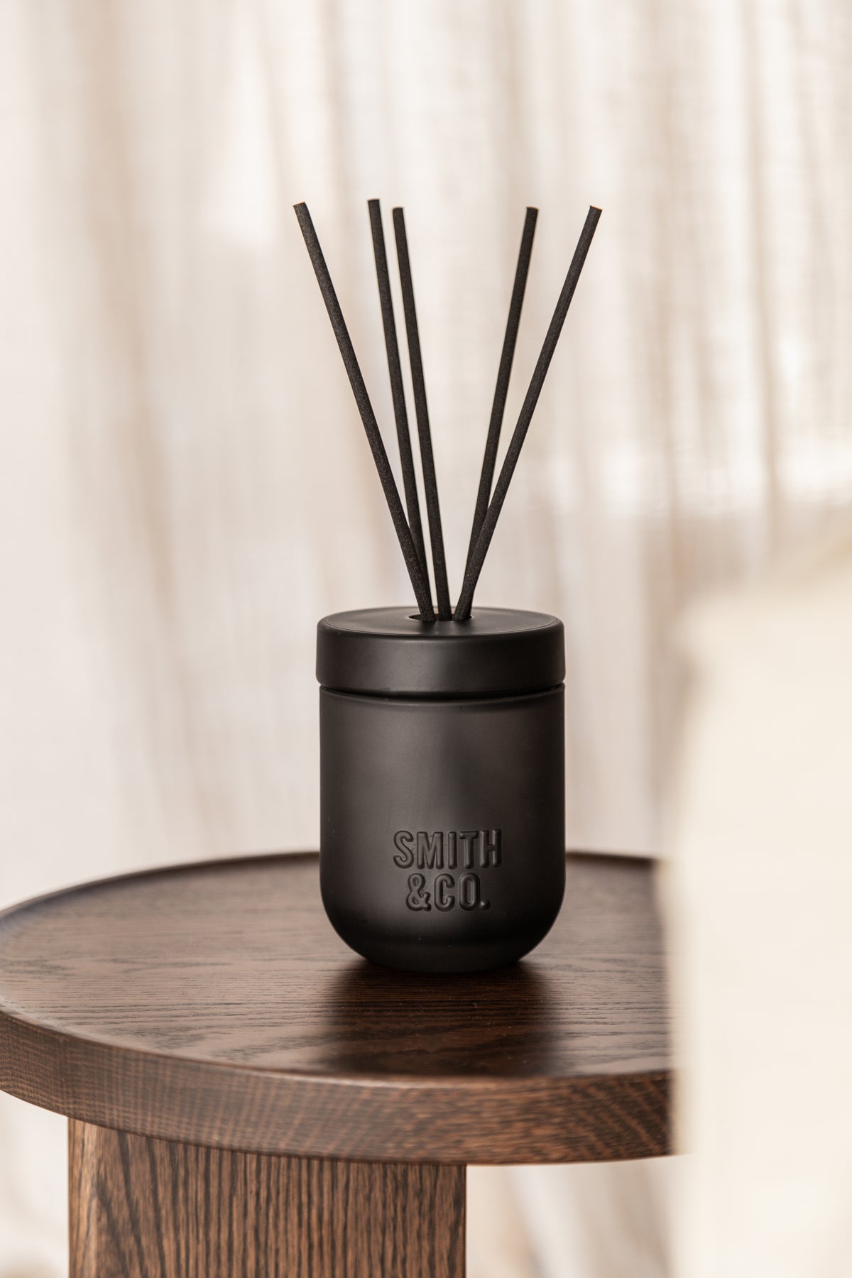 Close view of the Smith & Co. diffuser on a dark side table with sheer curtains behind