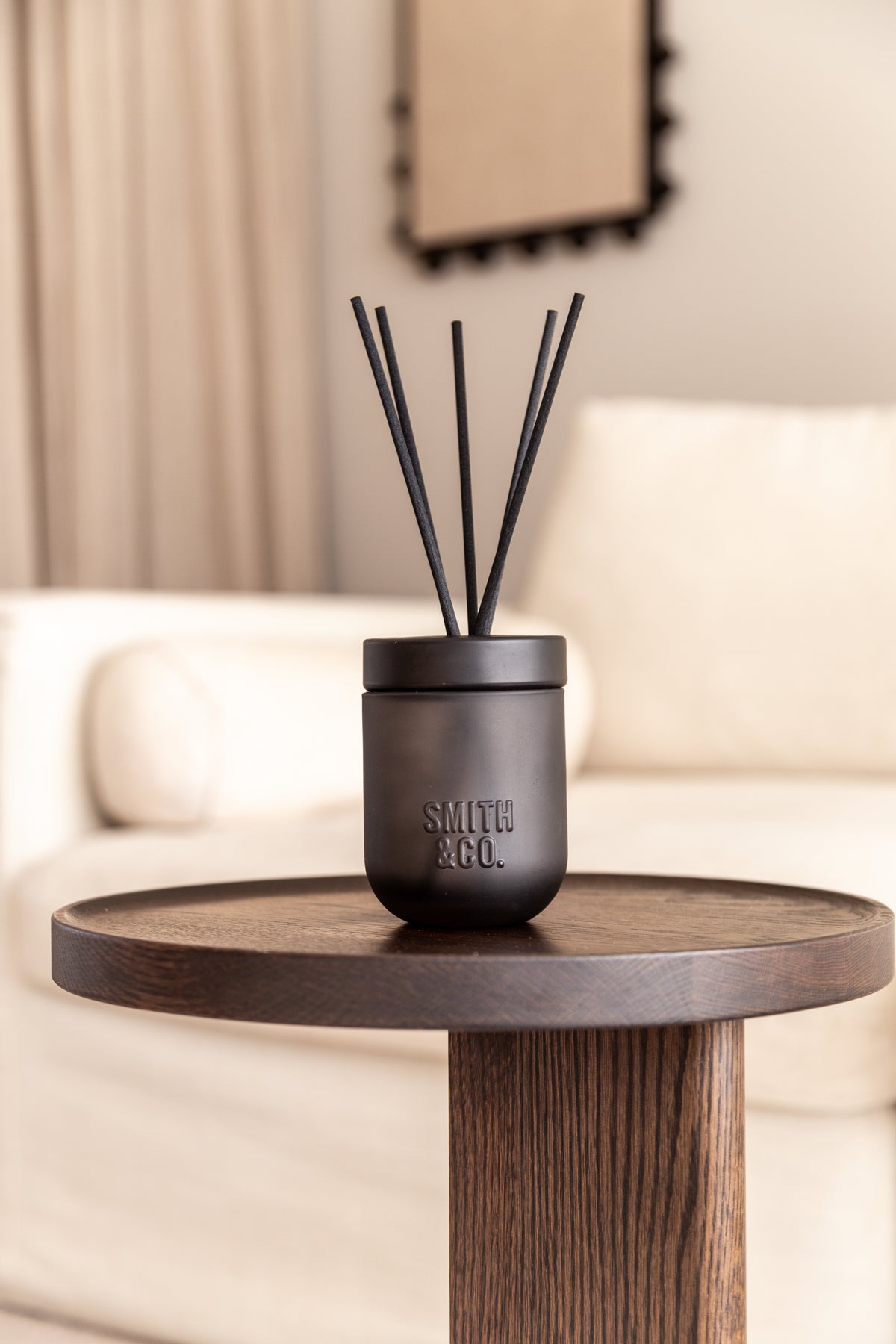 Smith & Co. diffuser on a dark round side table with a sofa and wall art behind