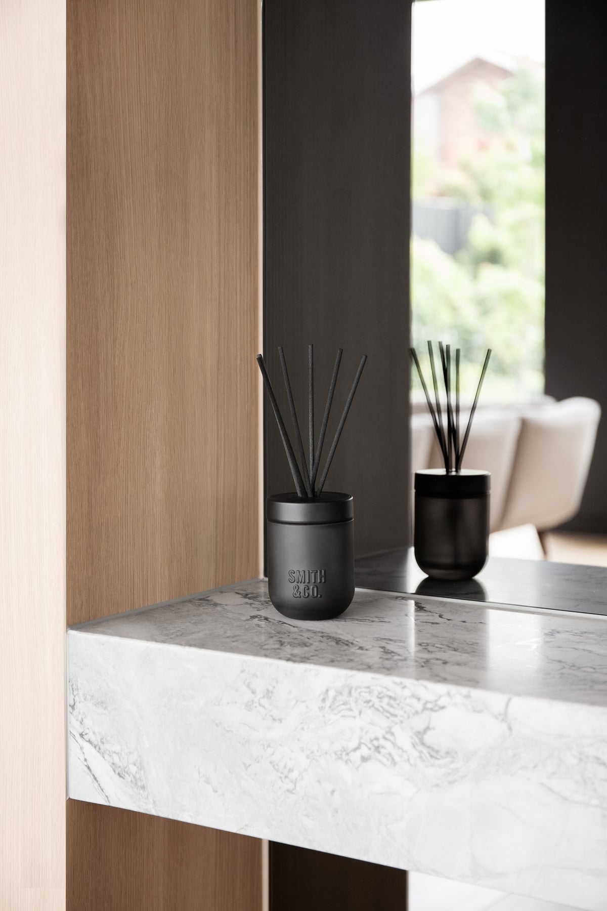 Wide view of two Smith & Co. diffusers on a marble ledge by timber and black walls