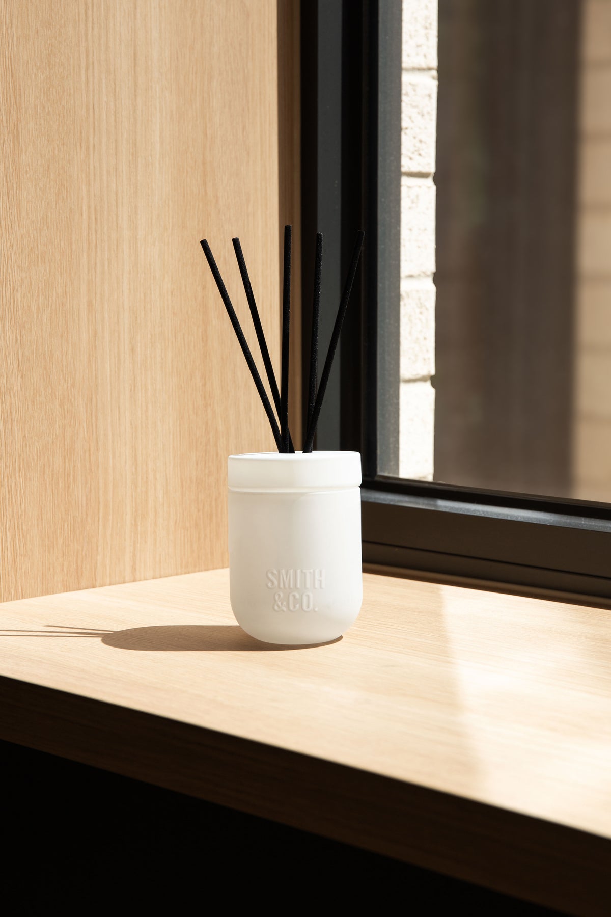 White Smith and Co diffuser on a sunlit timber window ledge beside a dark frame
