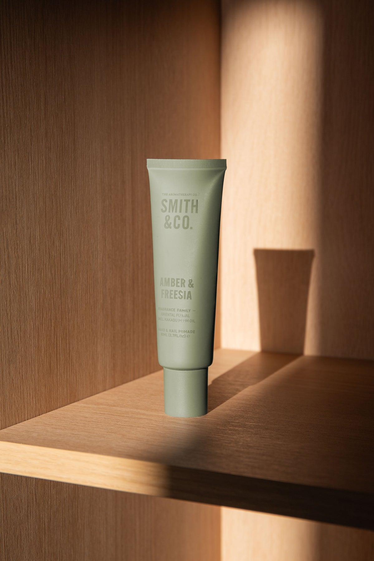 Front view of the sage green tube on a lower oak shelf with sunlight and shadow