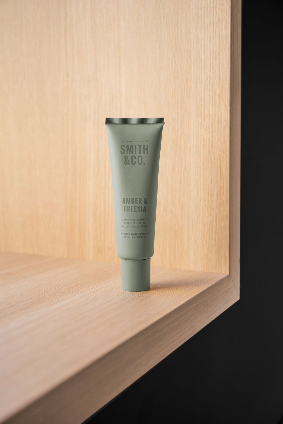 Sage green tube standing in the corner of an oak shelf beside a black panel