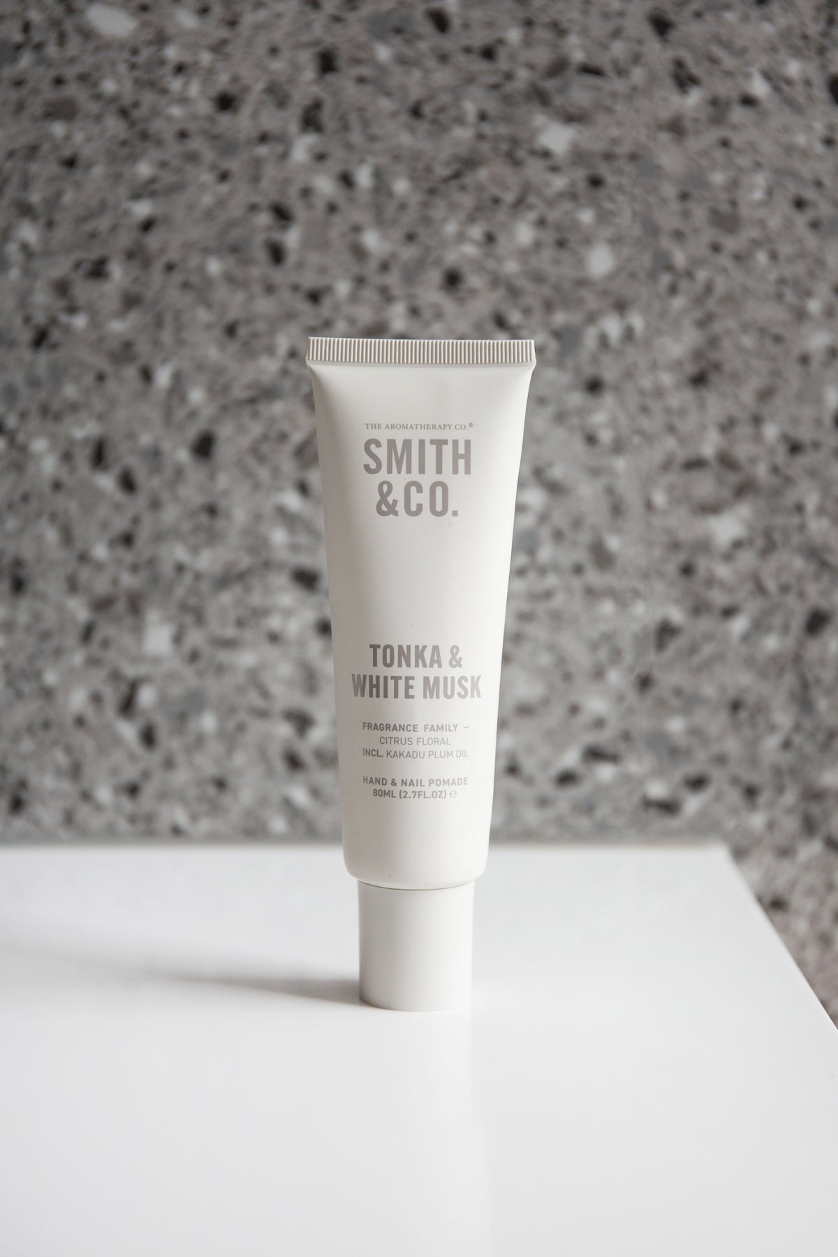 Hand cream tube standing on a white ledge against a grey terrazzo wall