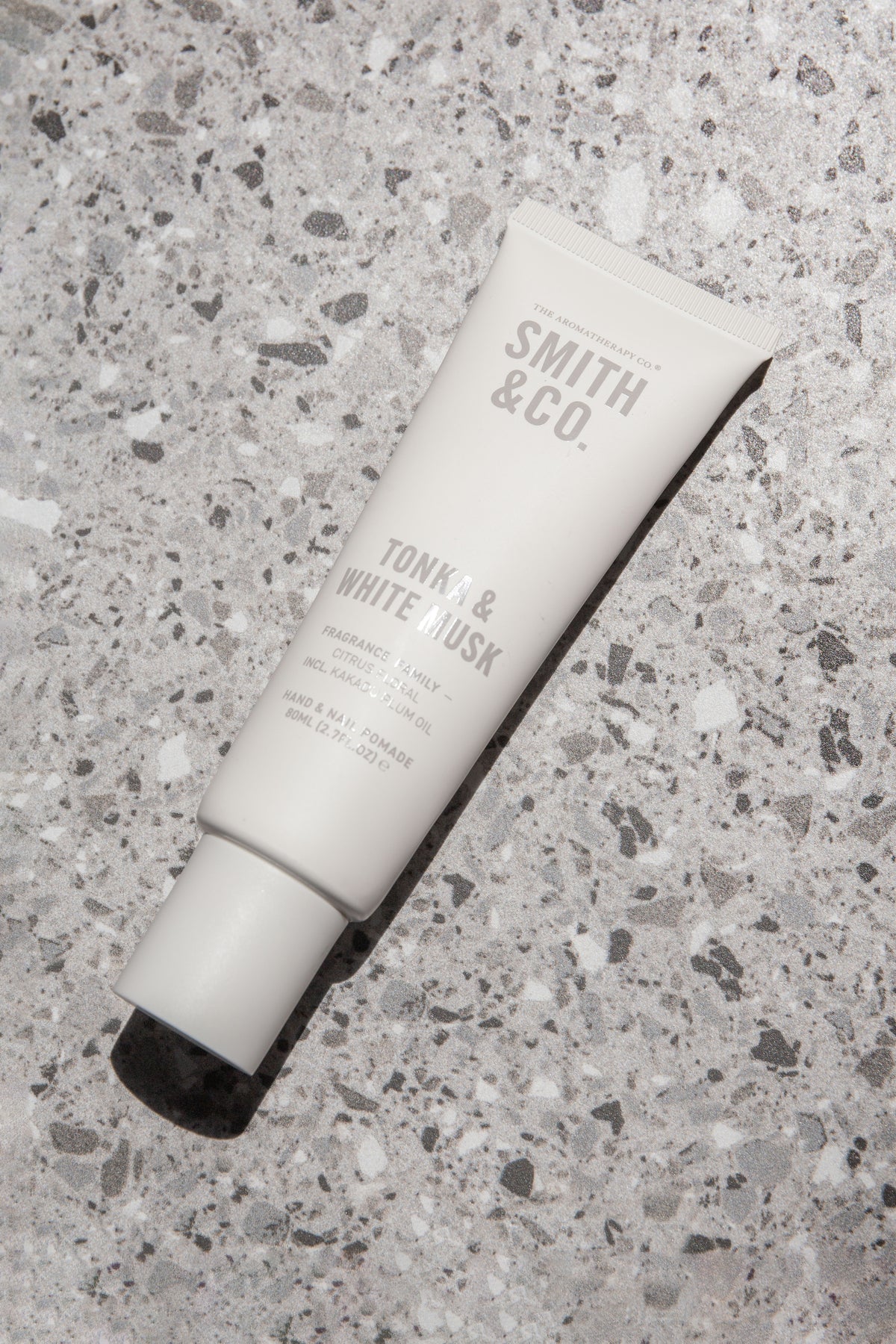 Hand cream tube lying at an angle across a grey terrazzo surface