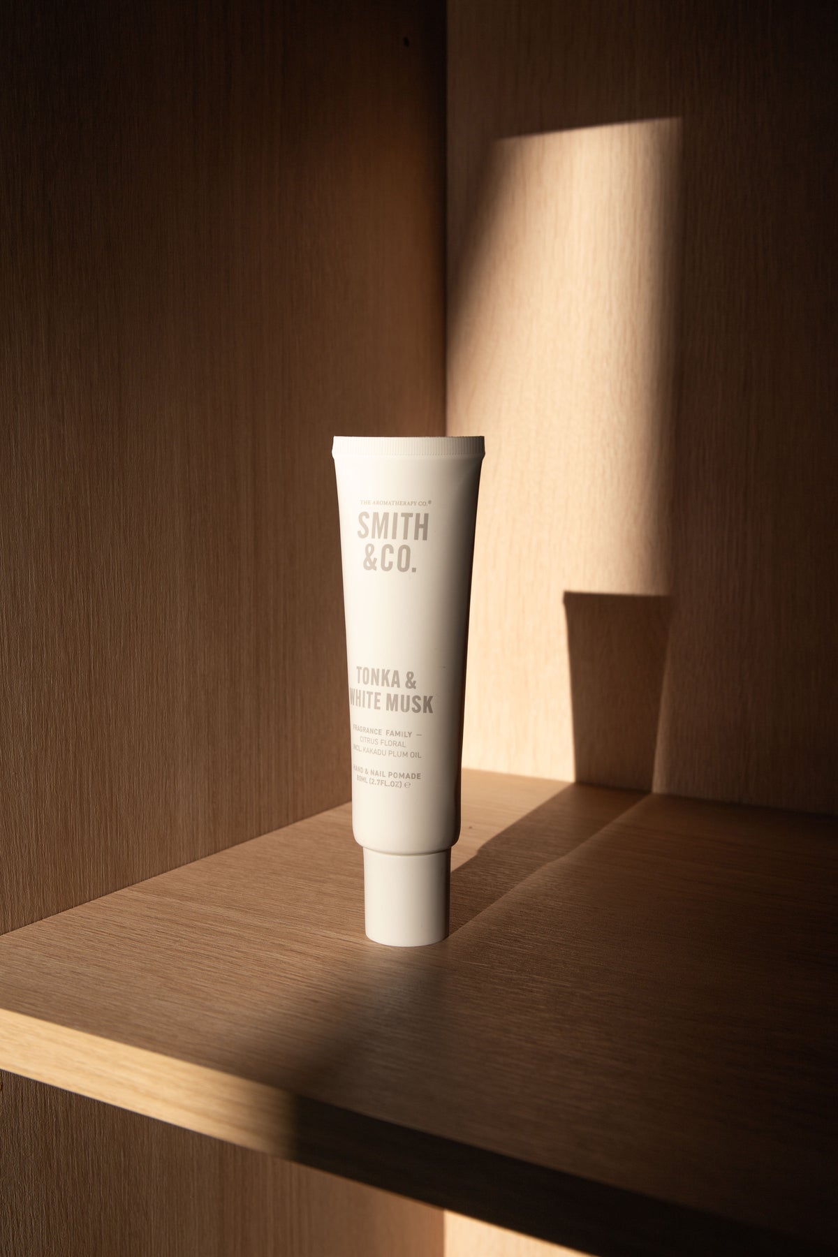 Hand cream tube on a timber shelf in a sunlit niche, warm shadows behind