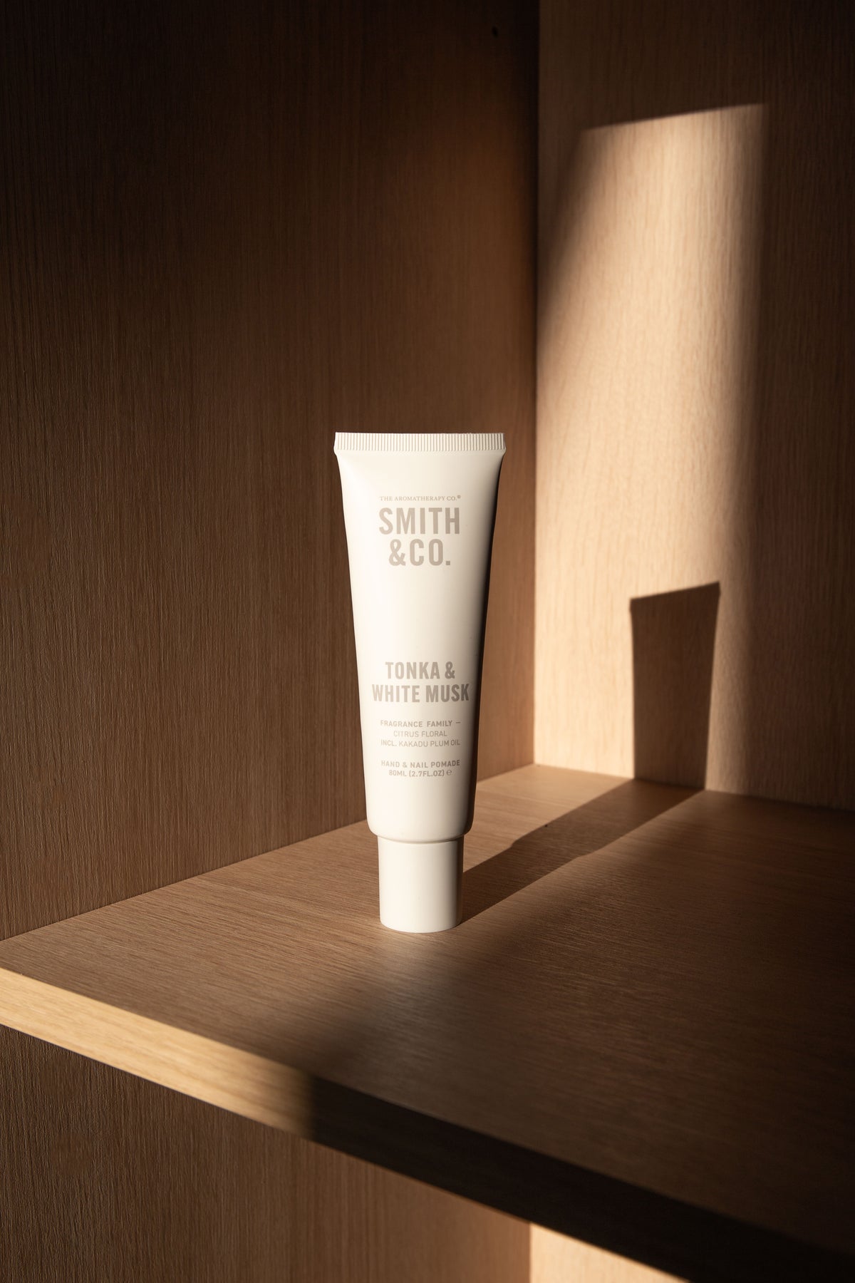Wider view of the hand cream tube on a timber shelf with a hard diagonal shadow