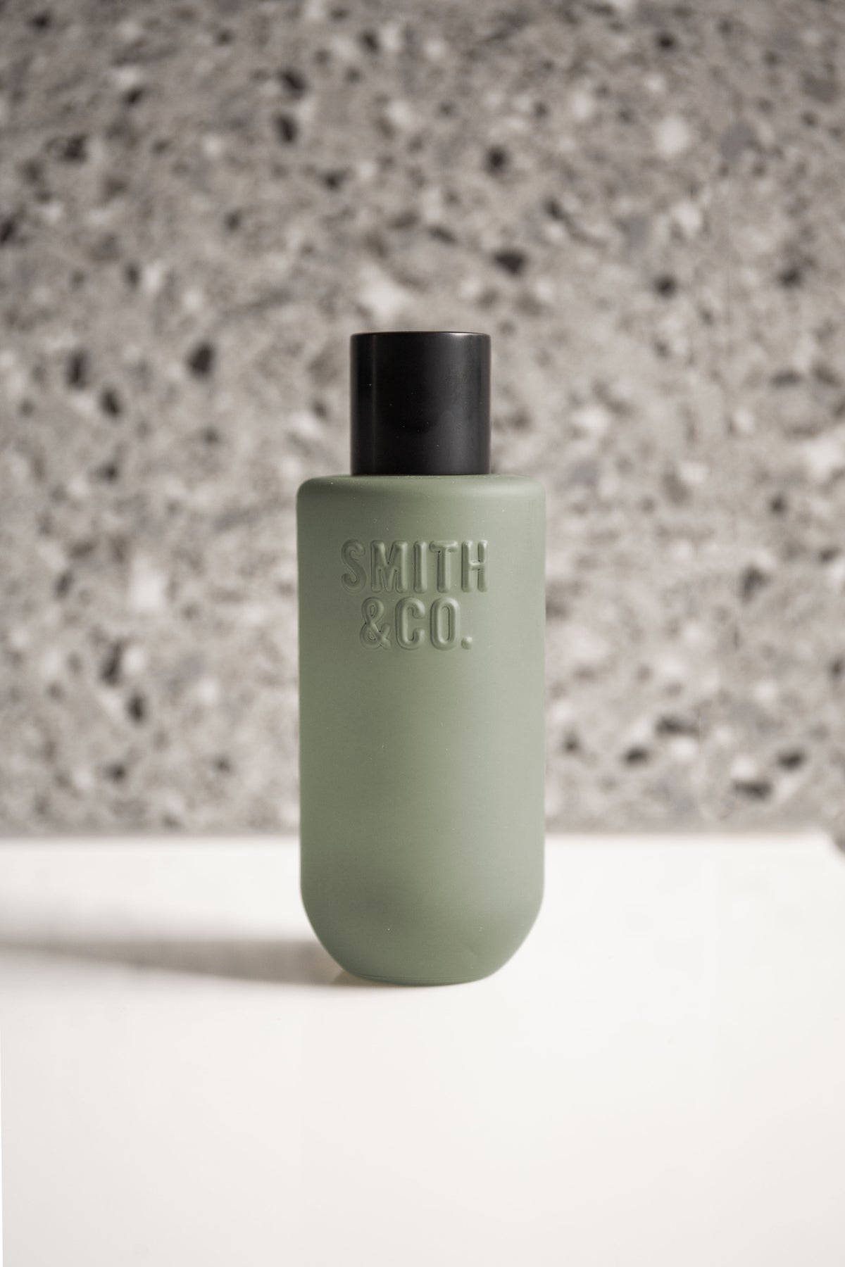 Close view of the room spray's embossed Smith & Co. logo against grey terrazzo