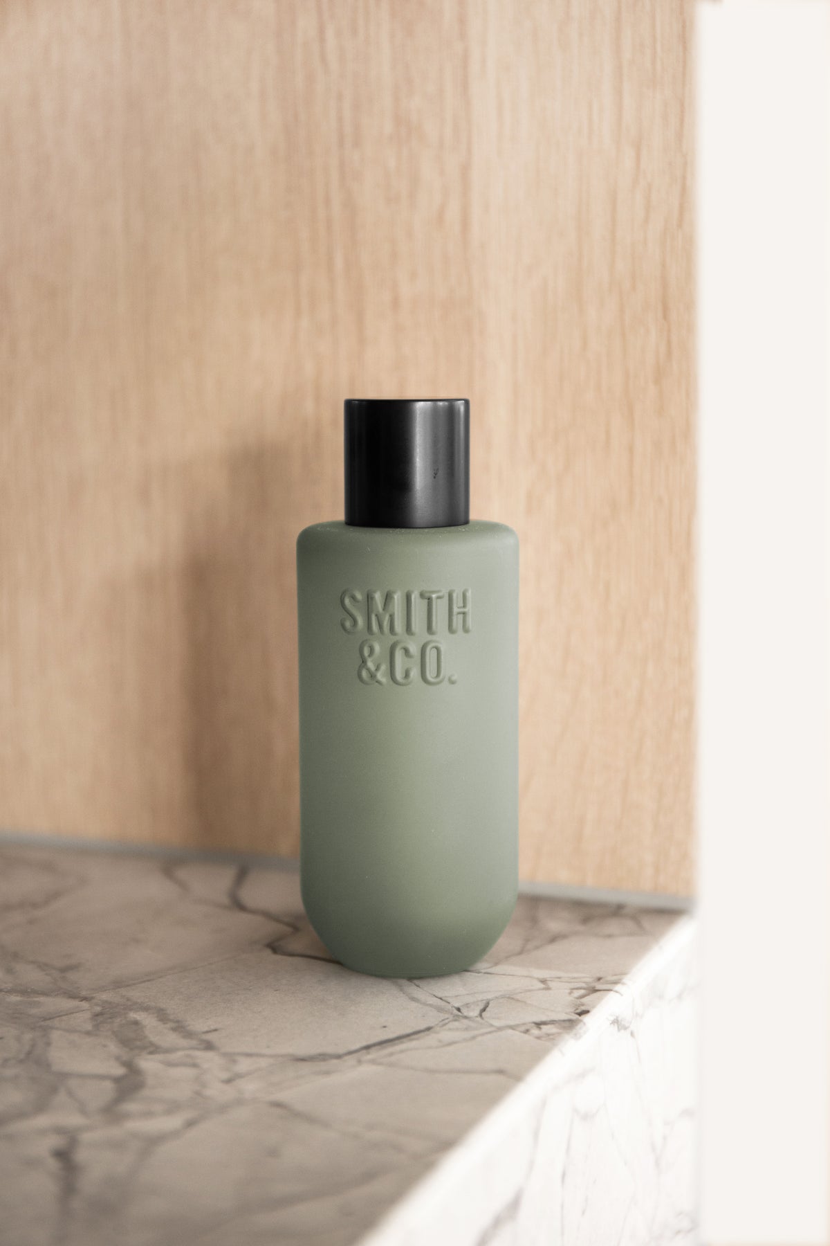 Sage green room spray on a veined marble ledge in front of an oak panel