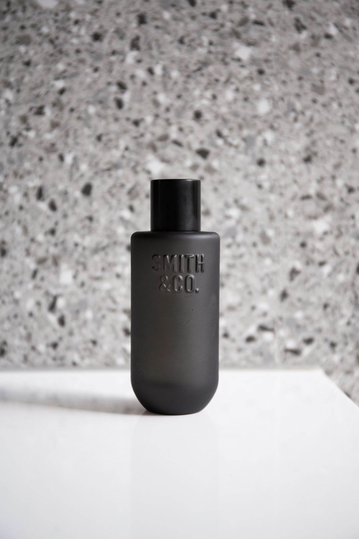 Black Smith and Co room spray on a white plinth in front of a terrazzo wall