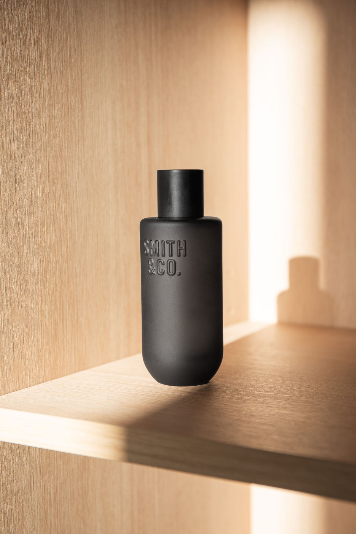 Black Smith and Co room spray on a pale timber shelf lit by a warm strip light
