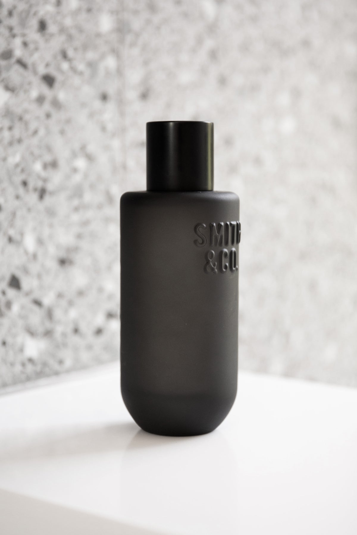 Close view of the black Smith and Co room spray on a white plinth against terrazzo