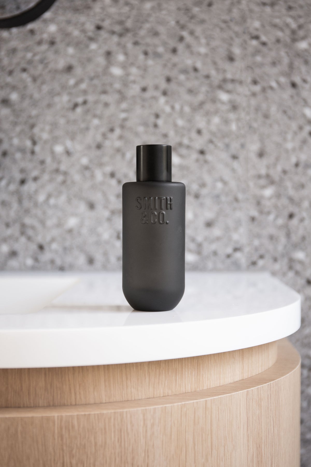 Black Smith and Co room spray on the edge of a round white basin against terrazzo