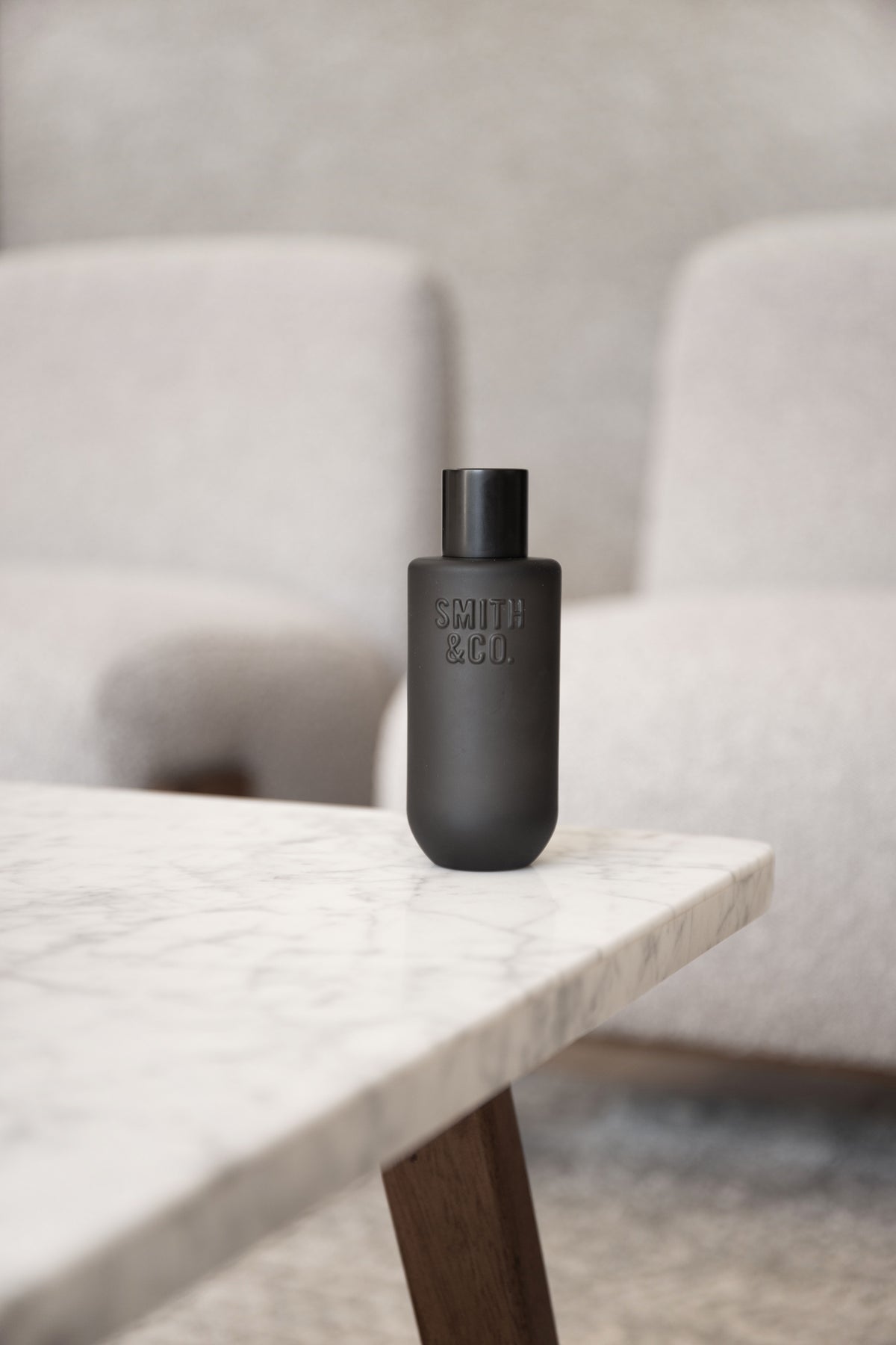 Black Smith and Co room spray on a marble bench edge with boucle chairs behind