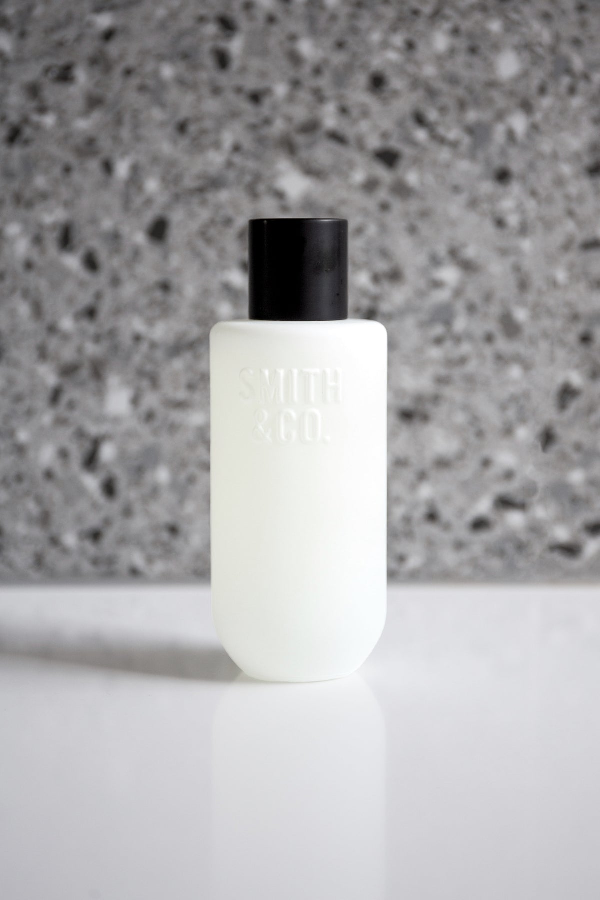 Room spray bottle centred on a white benchtop with grey terrazzo softly blurred behind