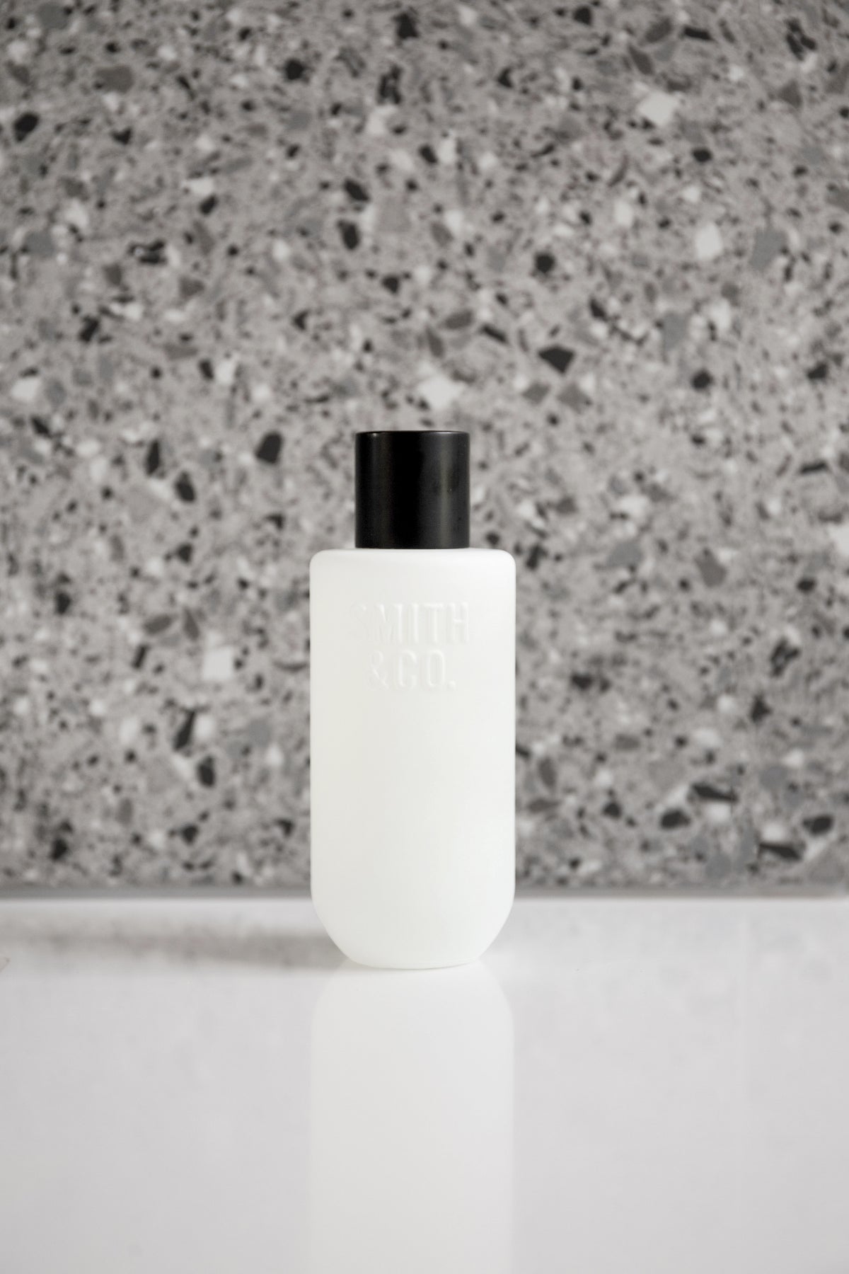 Frosted white room spray on a white surface with a grey terrazzo wall behind