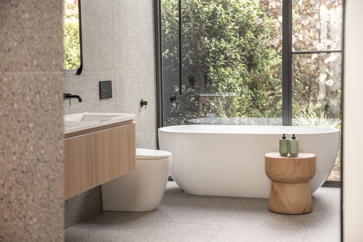 Bathroom with a floating timber vanity, freestanding bath and timber stool by a garden window