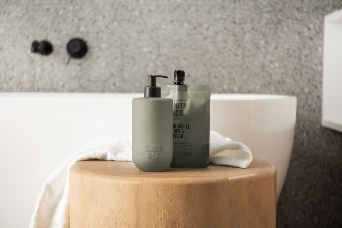 Sage green Smith & Co. bottles on a bath ledge beside black tapware