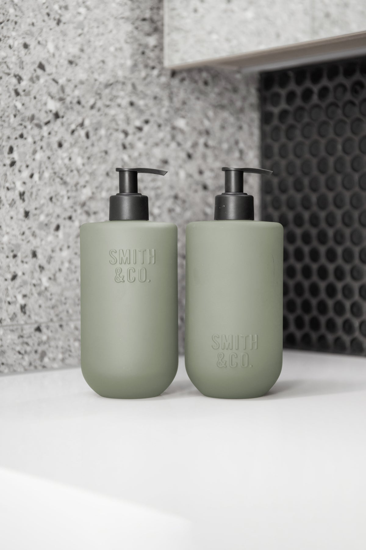 Two sage green bottles on a grey stone surface, close view