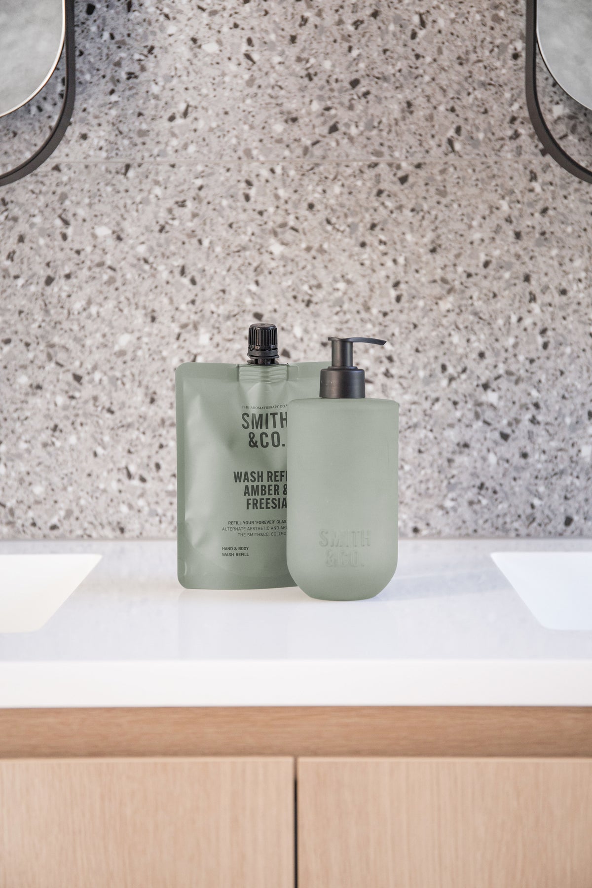 Sage green bottles on a terrazzo vanity with timber cabinetry below