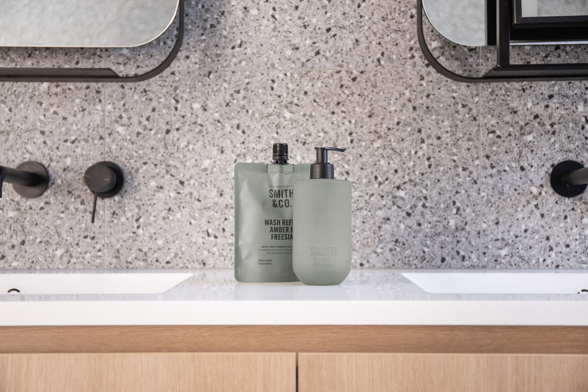Sage green bottles on a terrazzo vanity below a round mirror