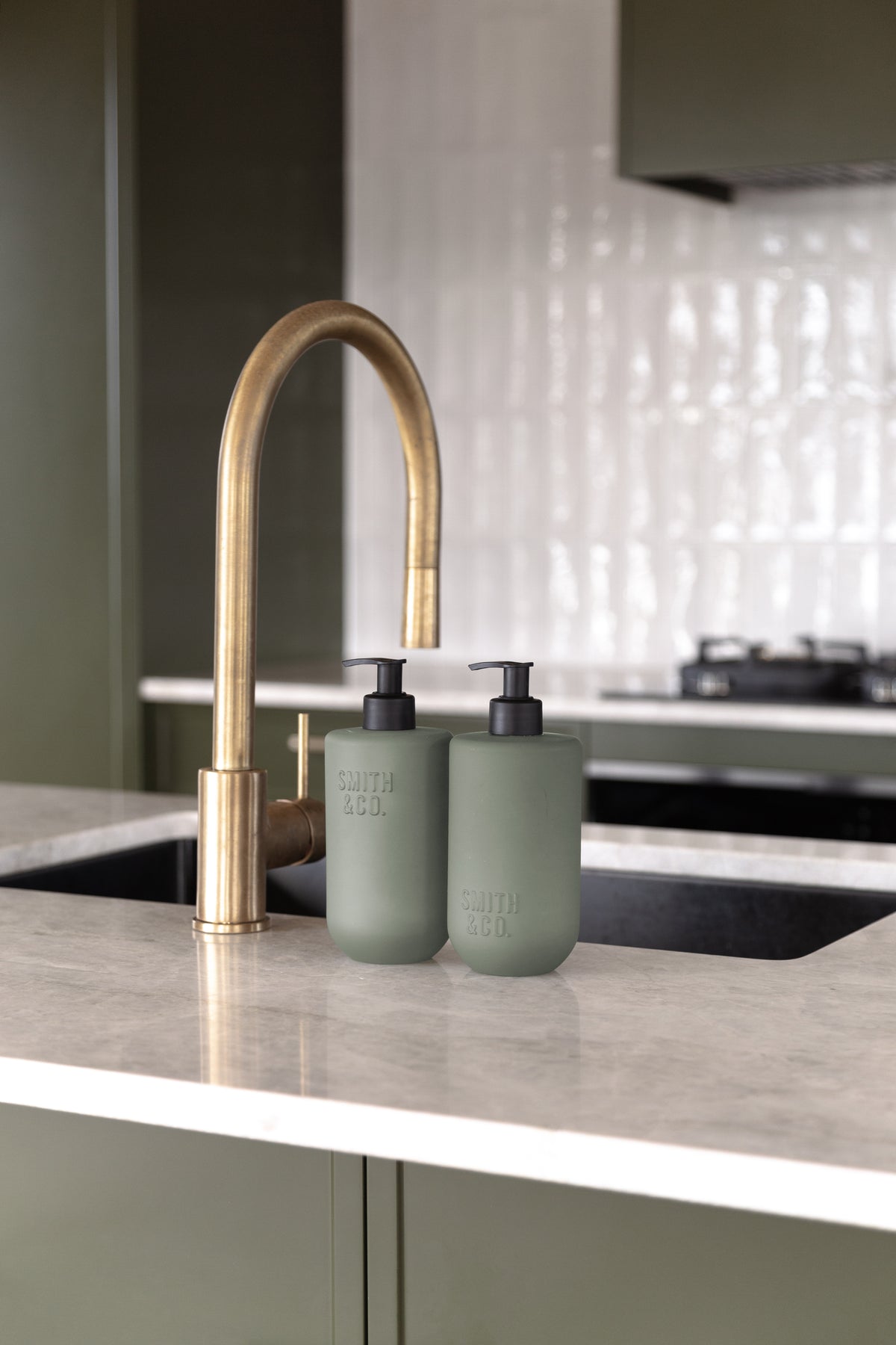 Sage green bottles by a brass tap with sage green cabinetry