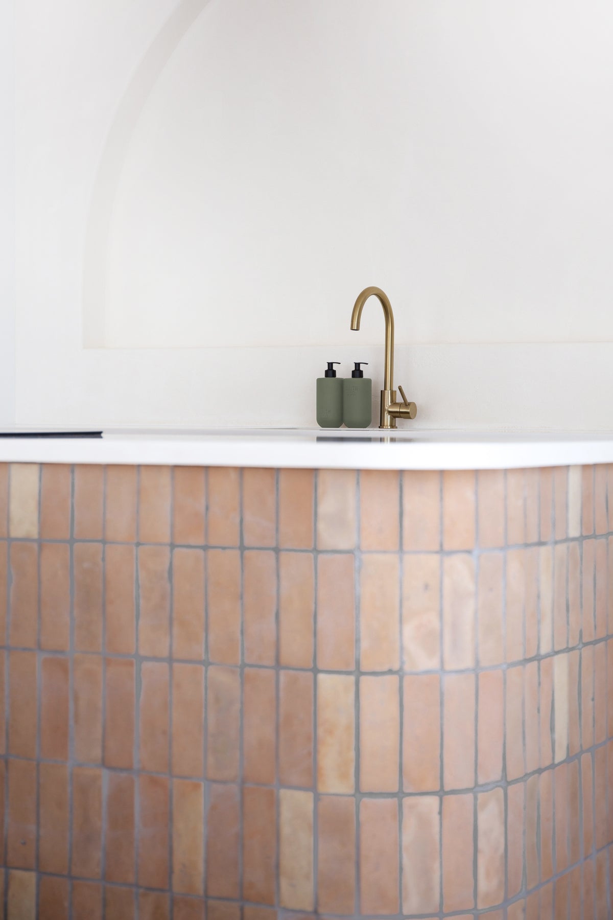 Brass tap on a pale basin with small Smith & Co. bottles, tiled vanity below
