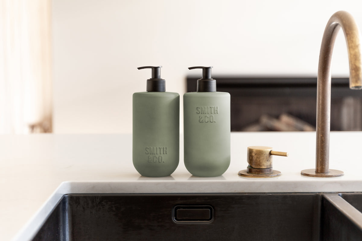 Close view of sage green bottles by a brass tap in a sink