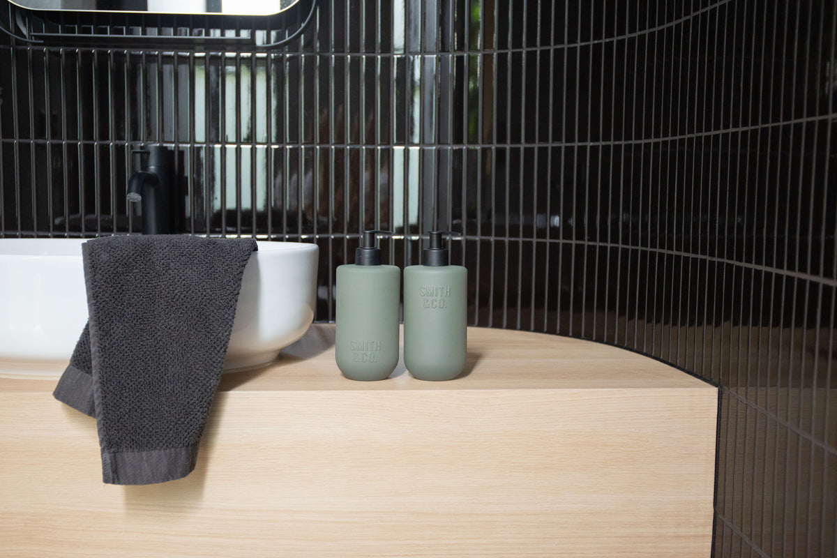 Sage green bottles and a towel against glossy black tiles