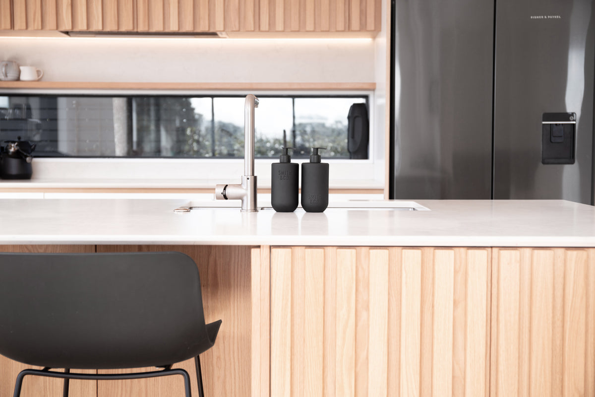 Kitchen with timber cabinetry and a black stool, with Smith & Co. bottles on the bench