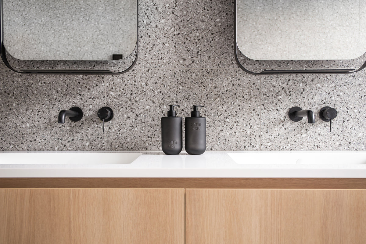 Two Smith & Co. bottles on a white vanity with black tapware and a terrazzo splashback
