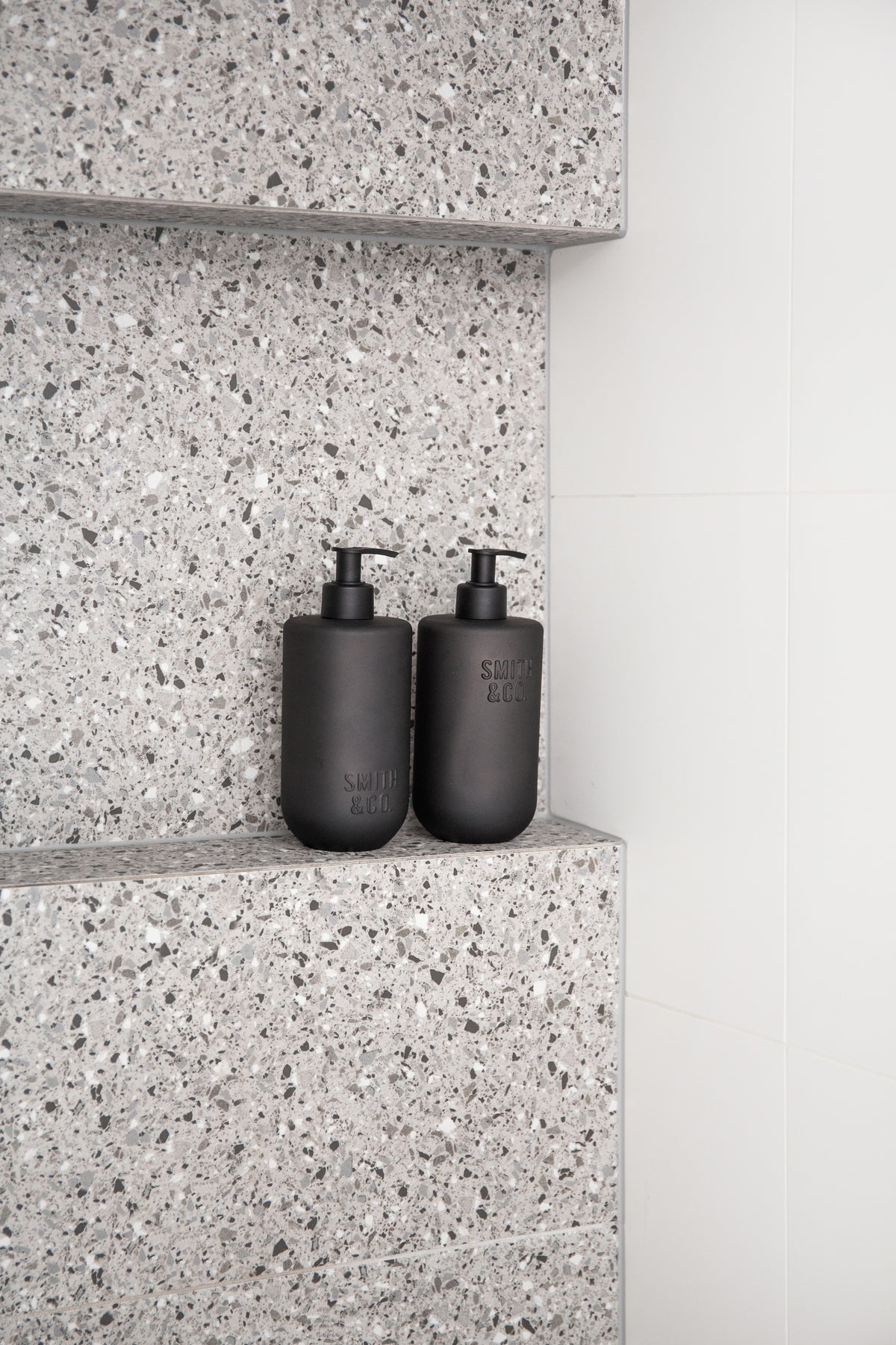 Two Smith & Co. bottles on a terrazzo shelf in a shower recess beside a white wall