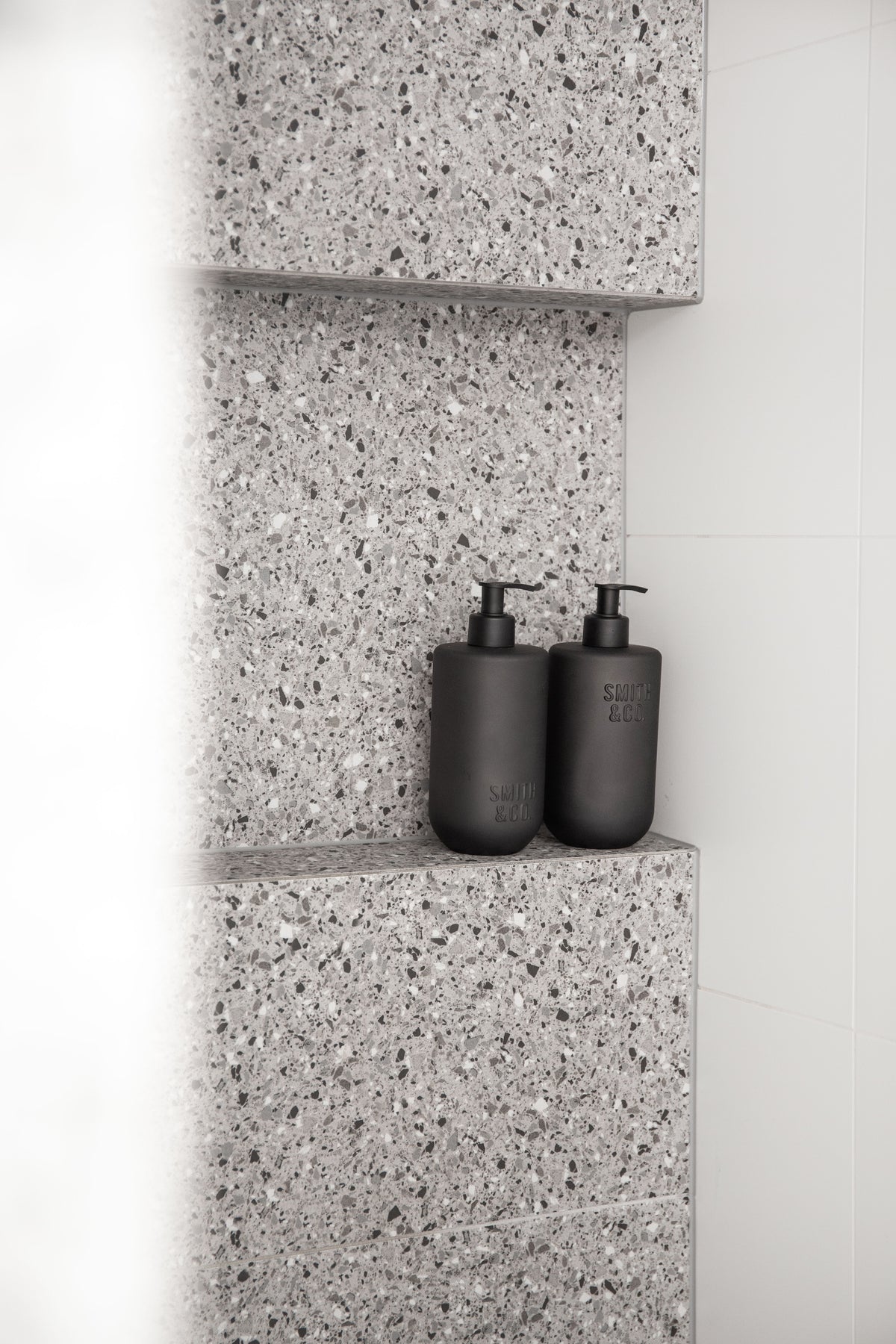 Two Smith & Co. bottles on a terrazzo shelf in a bright shower recess