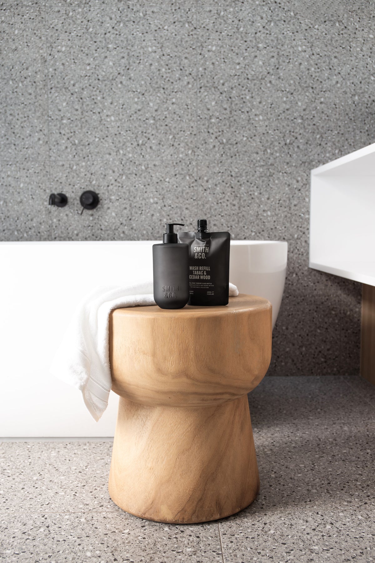 Smith & Co. bottle and refill on a timber stool in a grey shower