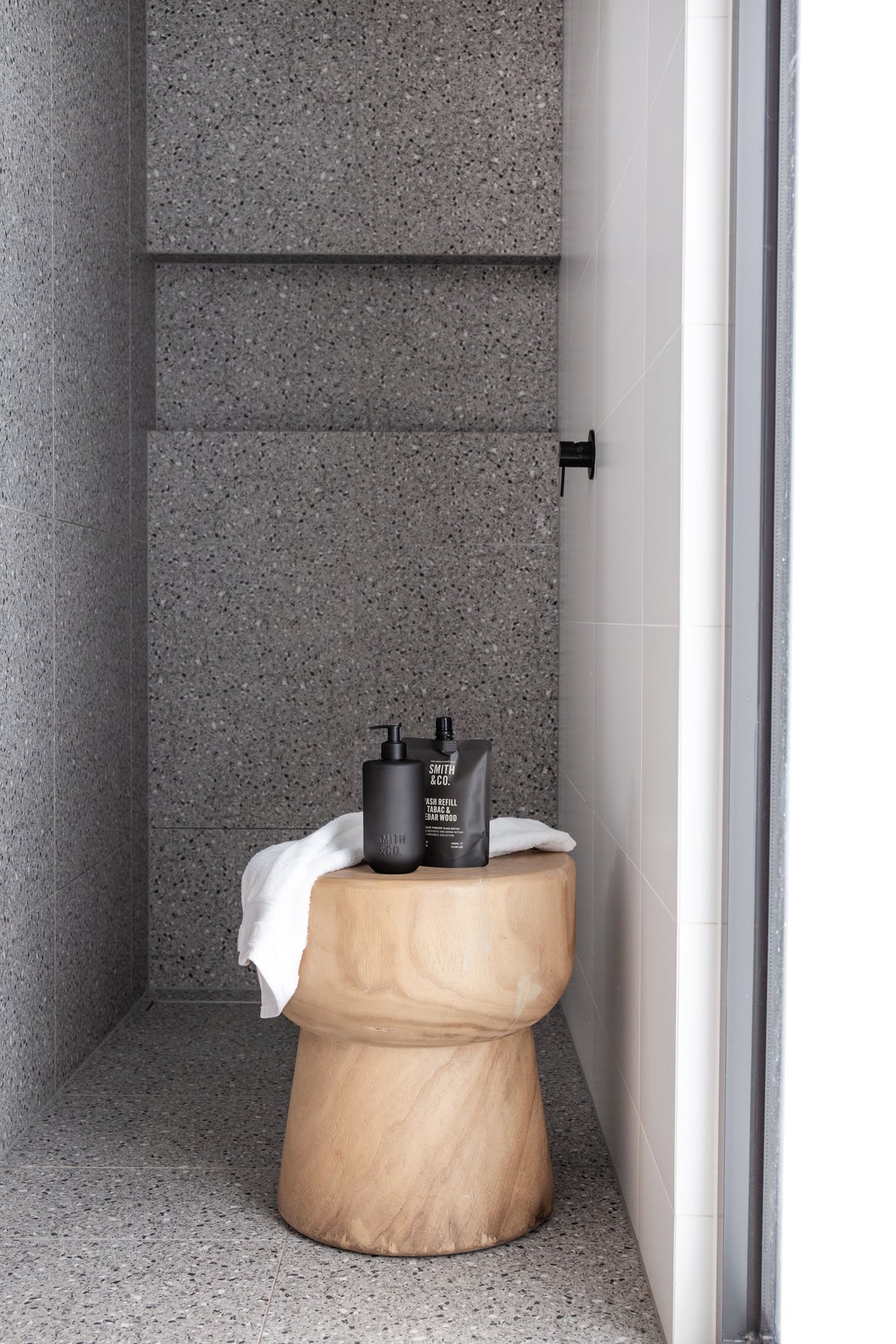 Smith & Co. bottles and a folded towel on a timber stool in a concrete shower