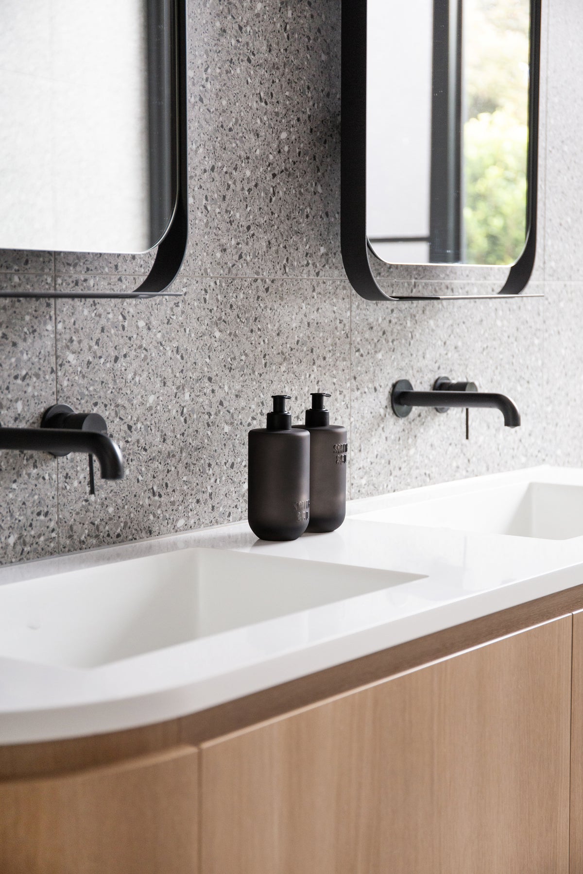 Curved timber vanity with twin mirrors and a Smith & Co. bottle on the basin top