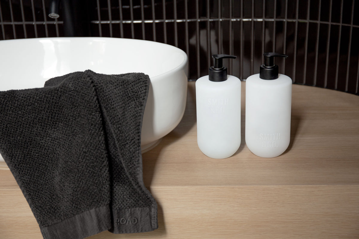 Two Smith and Co bottles on a timber ledge beside a bath with a dark towel
