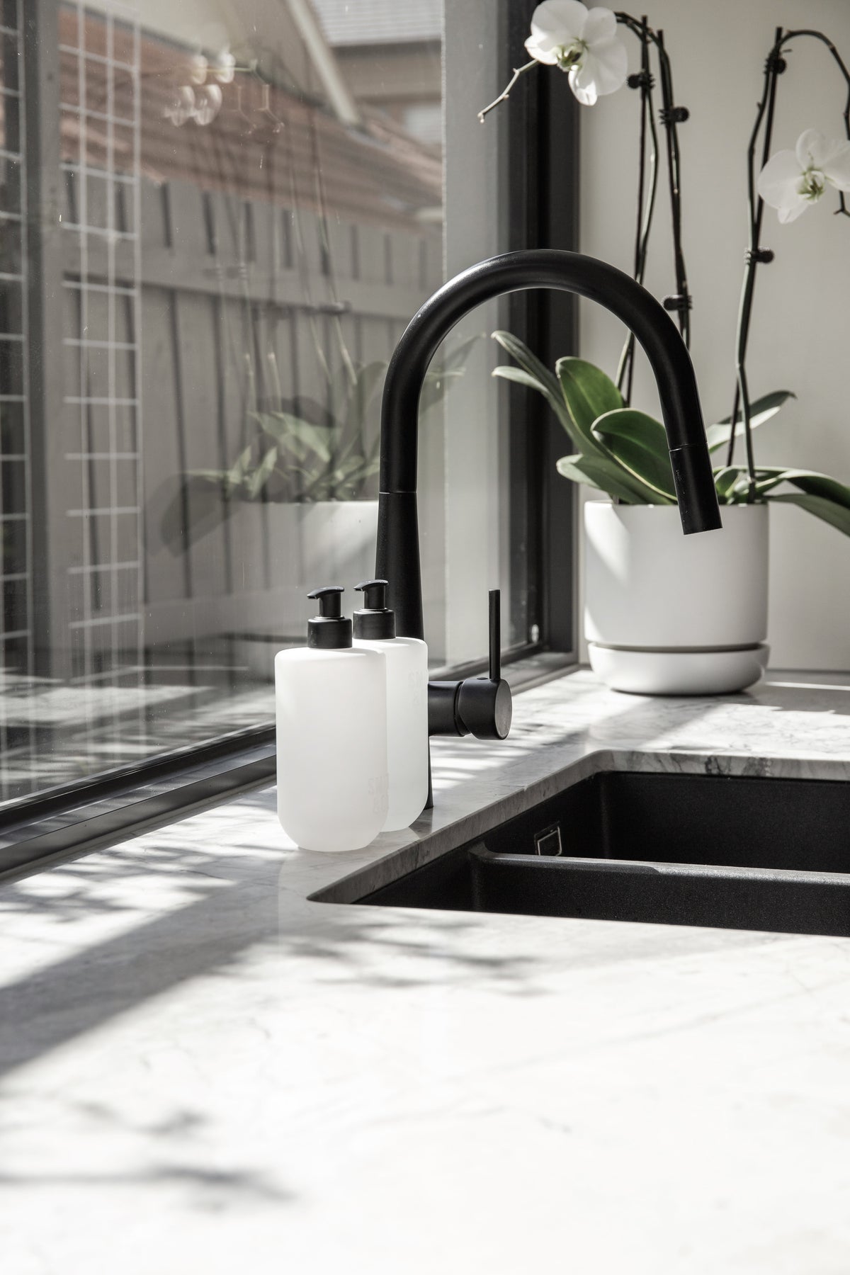 Frosted bottles beside a black tap on a marble bench with an orchid behind