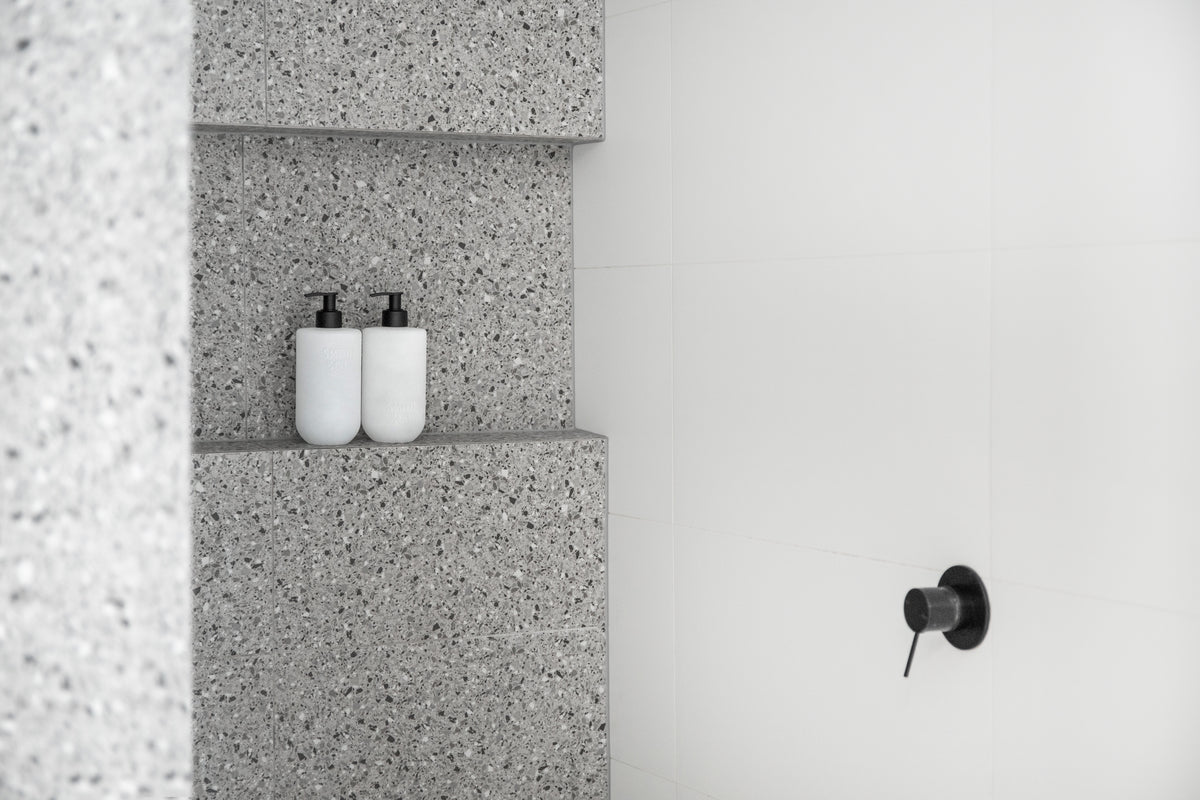 Landscape view of two Smith & Co. bottles in a terrazzo shower niche beside a black mixer