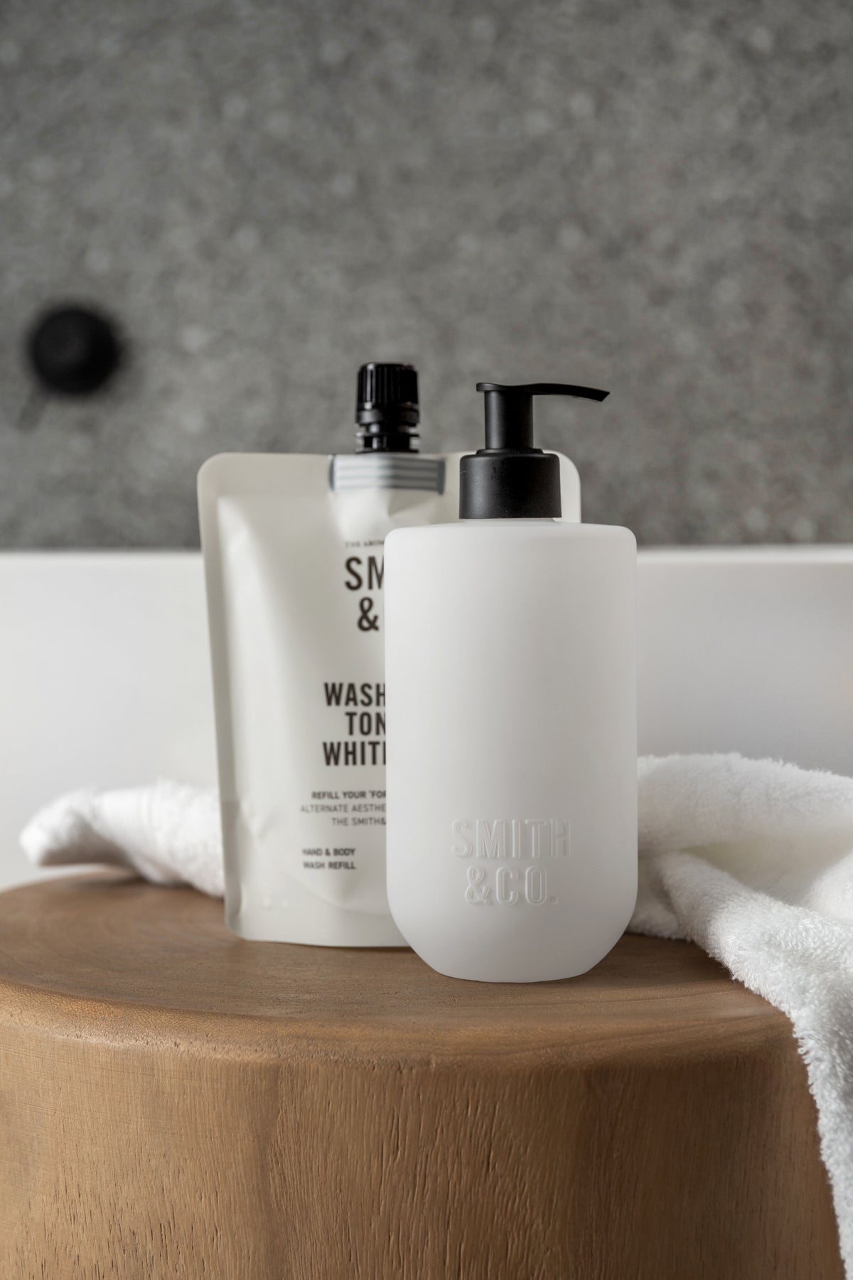 Smith & Co. wash bottle and refill pouch with a white towel on a timber stool, close view