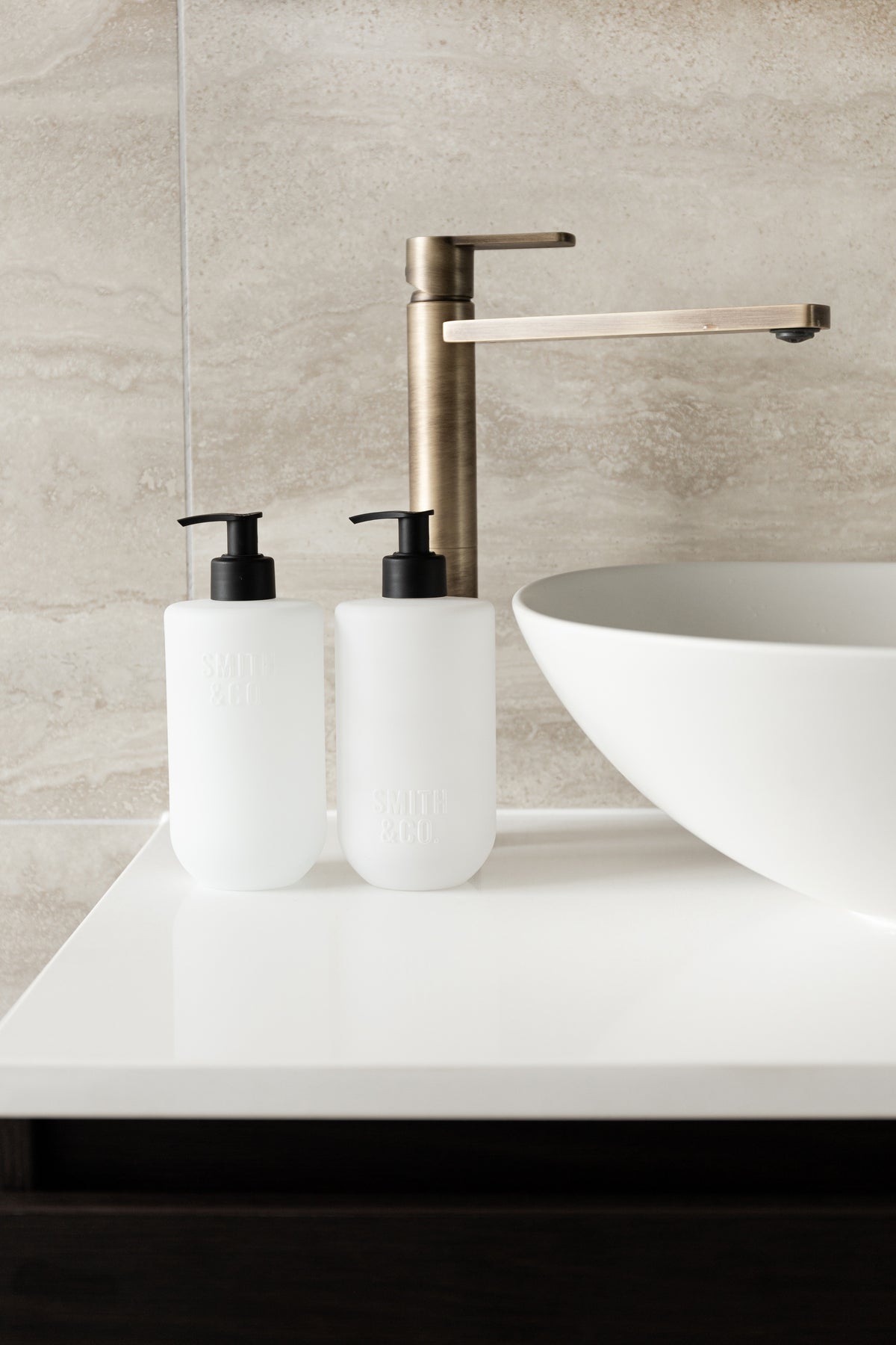 Two Smith and Co bottles beside a white basin with brass tapware