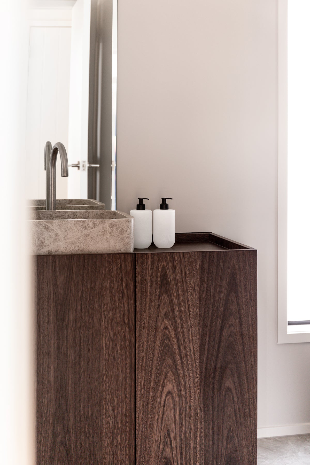 Two frosted bottles on a dark timber vanity next to a stone basin and a tall mirror