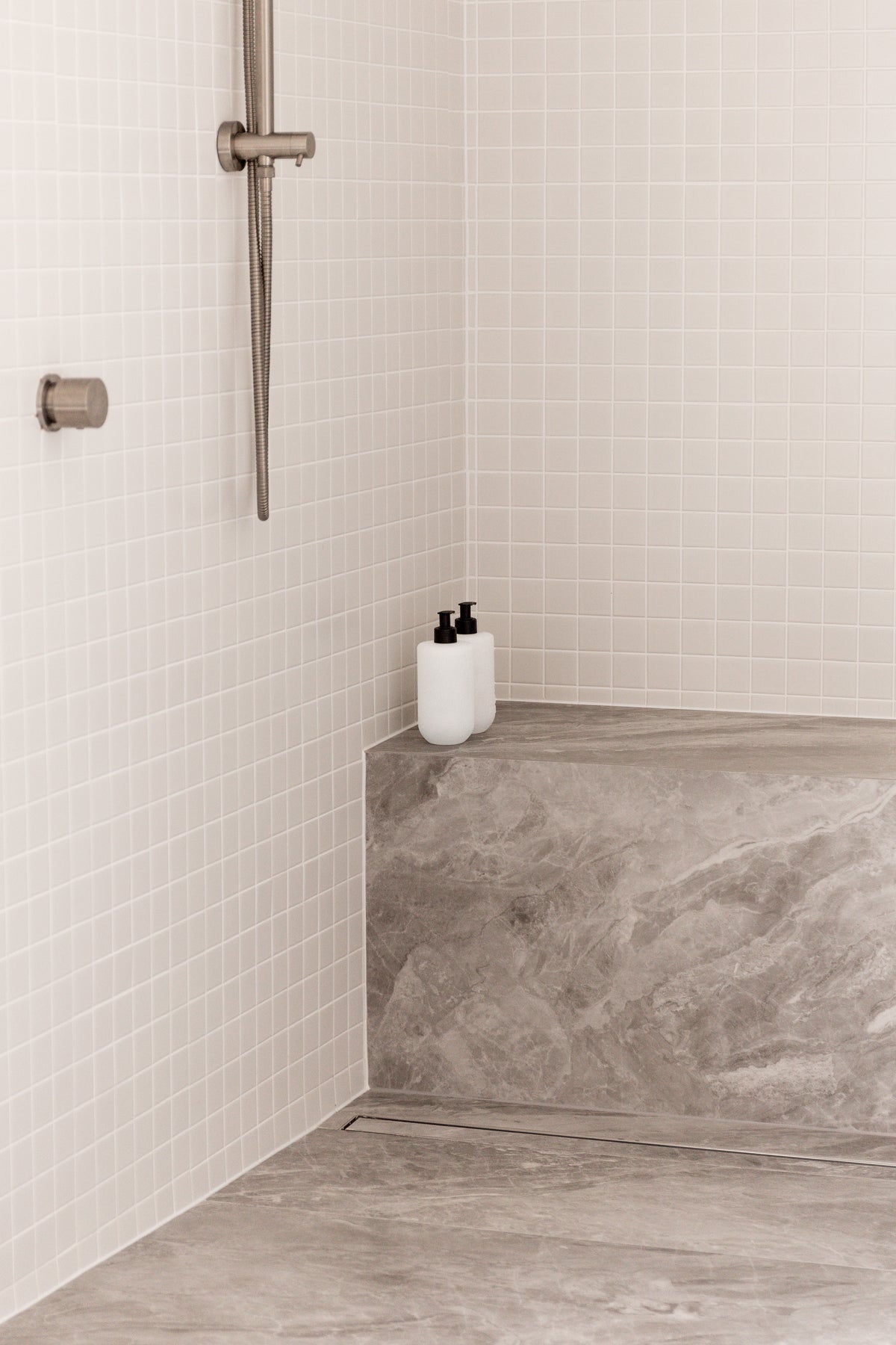 Smith & Co. bottles on a stone shower seat in a pale tiled shower with a brass rail