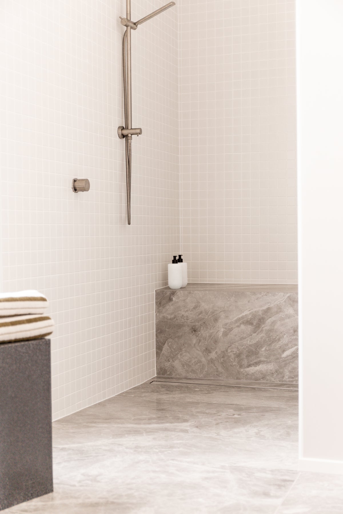 Tiled walk-in shower with a stone bench and two bottles, a striped towel on a stool in the foreground