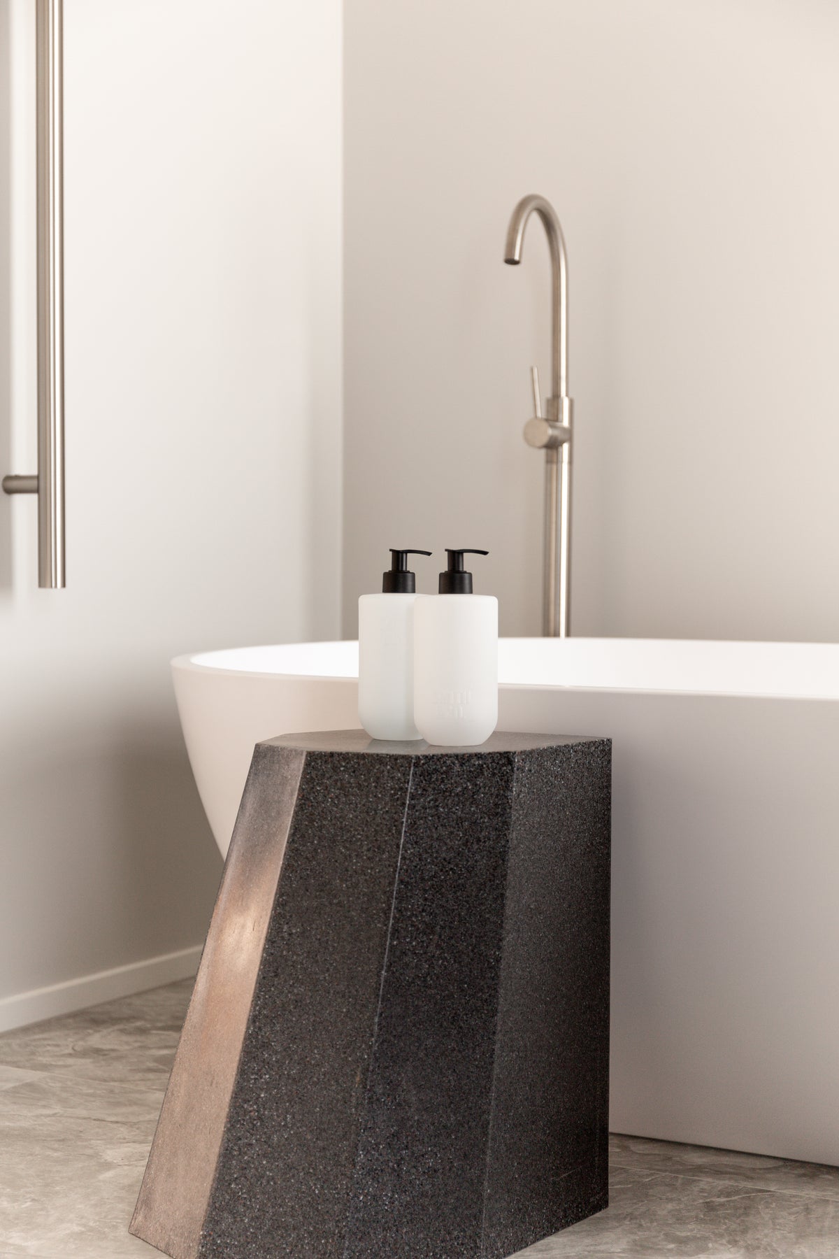 Smith & Co. bottles on a dark stool beside a freestanding bath with a brass floor mixer