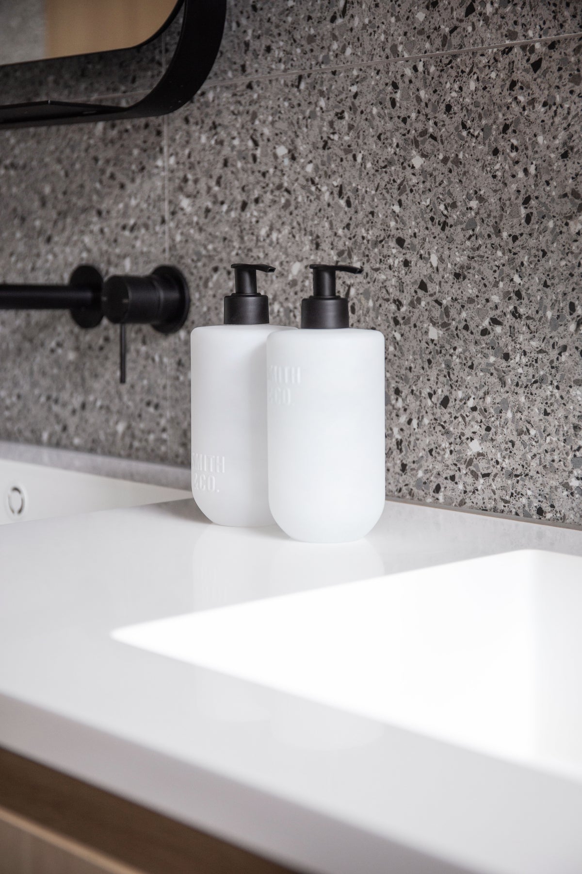 Smith & Co. bottles on a white vanity under a black framed mirror, terrazzo behind