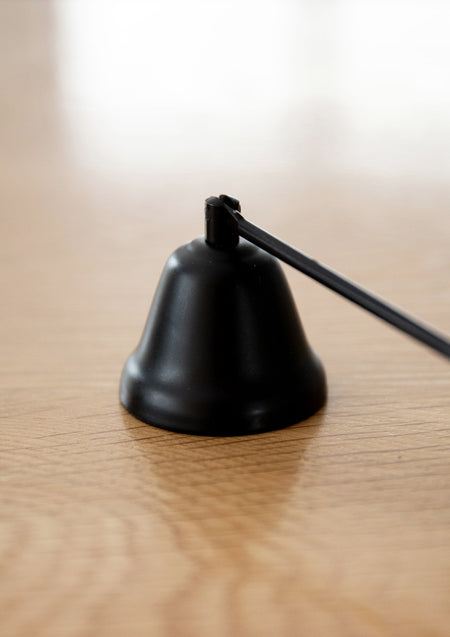 Close up of the black candle snuffer bell resting on light oak