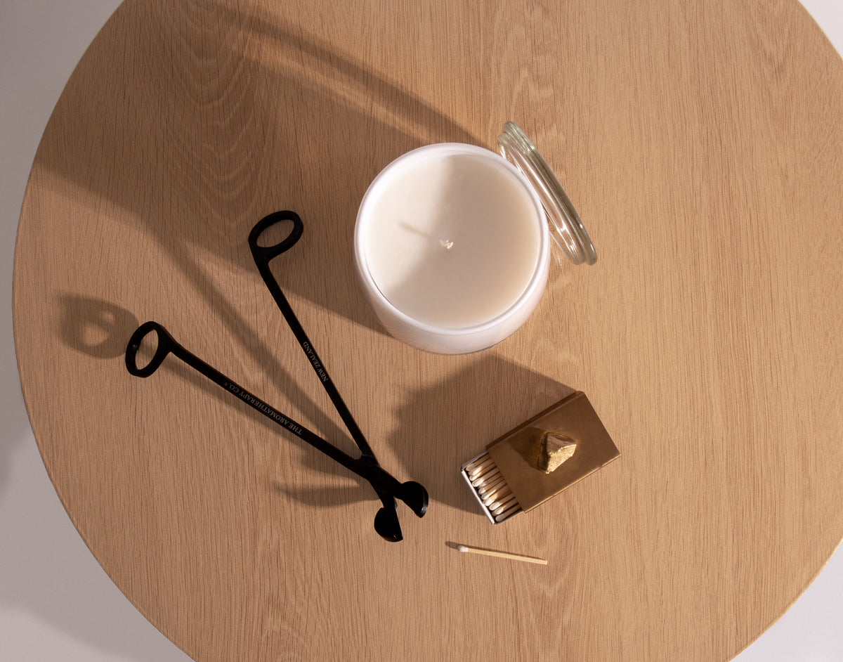 Top view of a Therapy candle, wick trimmer and snuffer on a round timber table