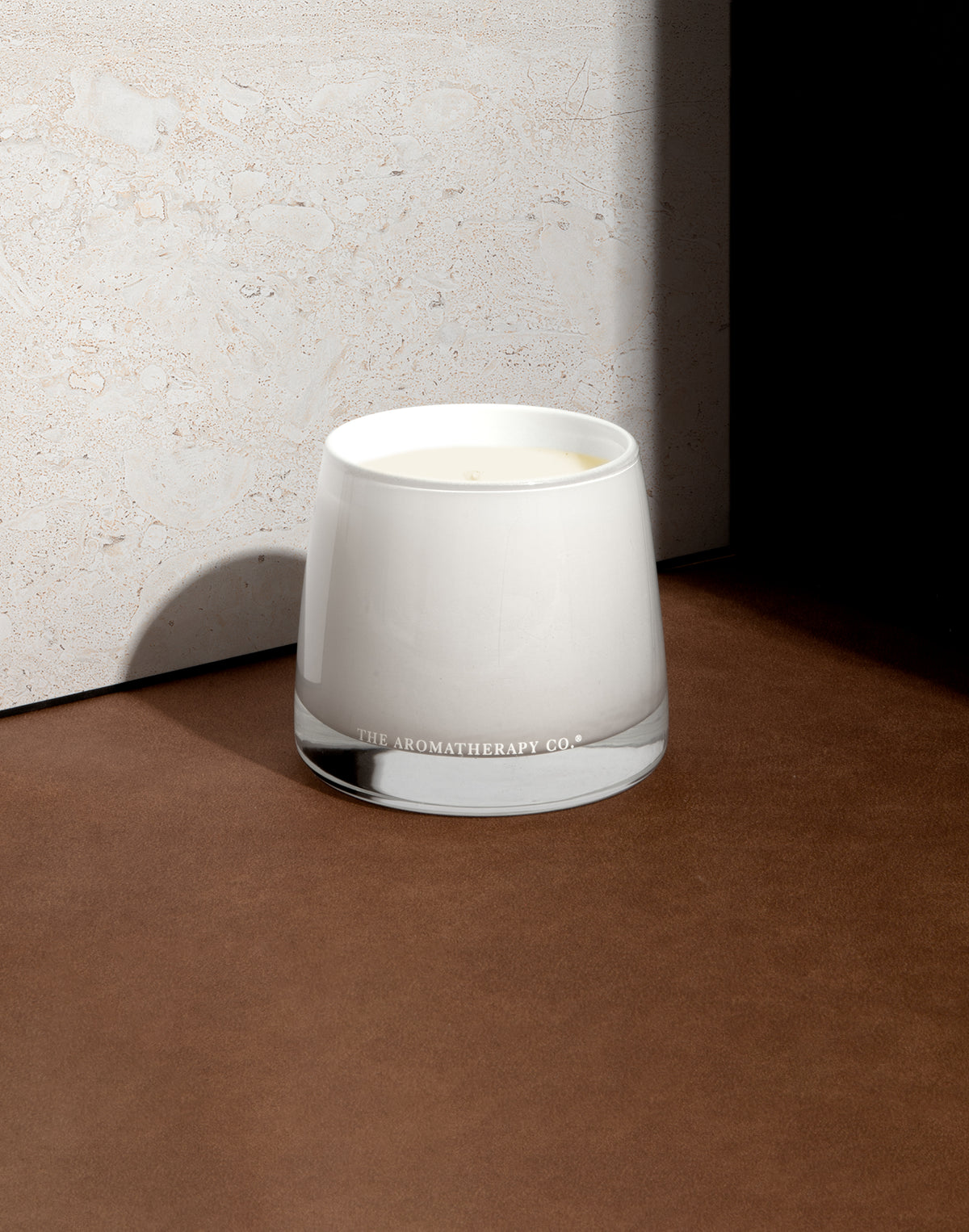 White glass candle in the corner of a brown ledge against a pale concrete wall